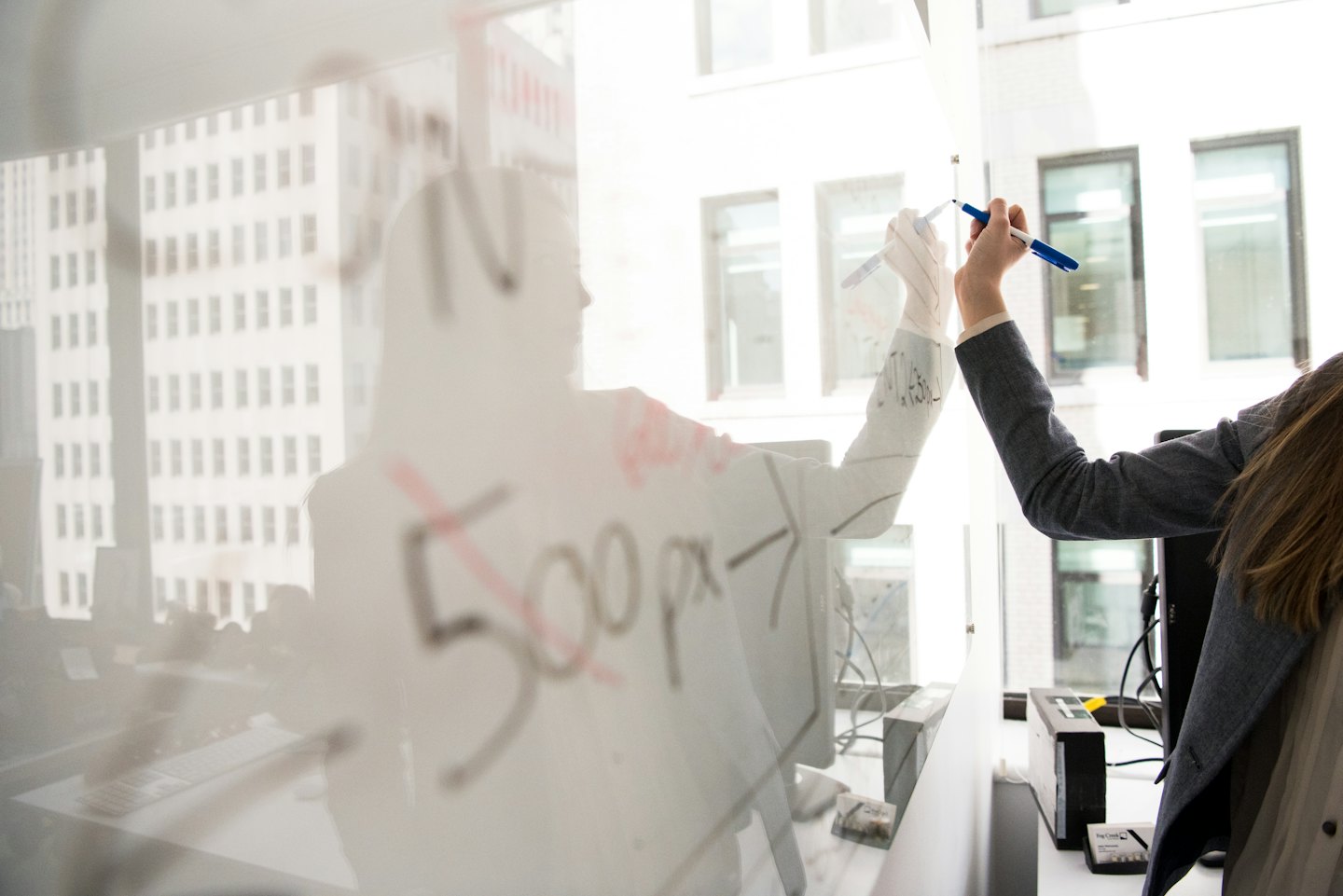Person schreibt auf Glaswhiteboard mit Stadtsspiegelung.